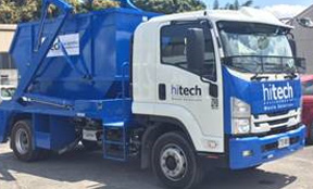 photo of a truck carrying a large blue skip waste bin